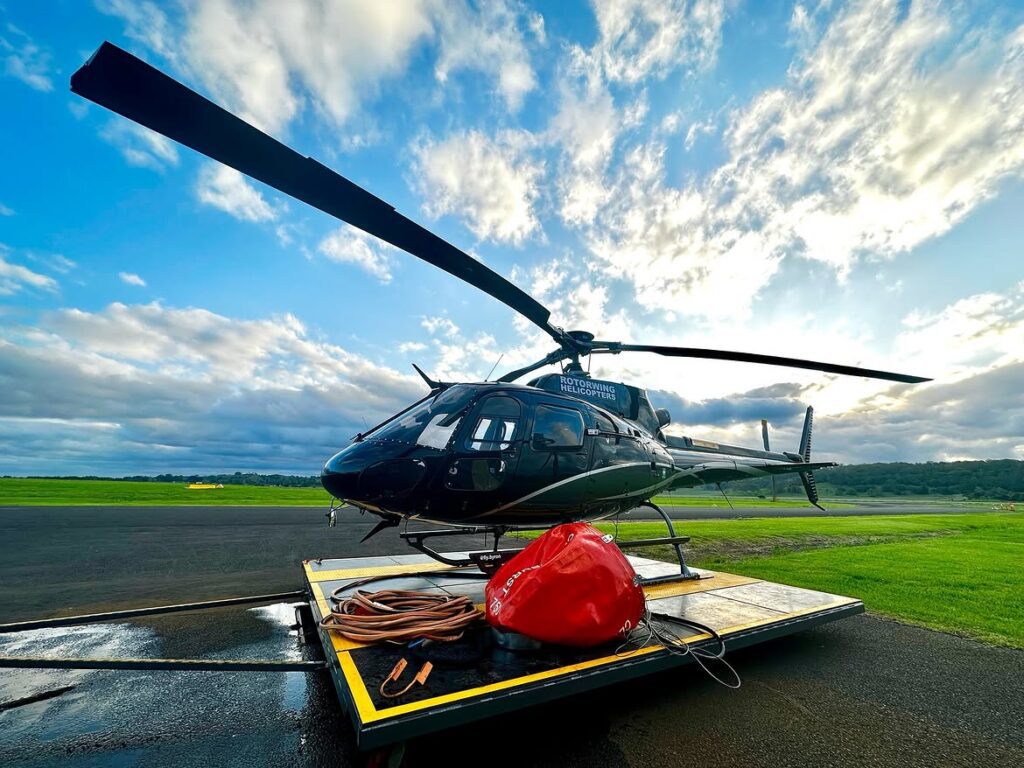 Staged commercial firefighting helicopter positioned on a helipad with a collapsible monsoon bucket.