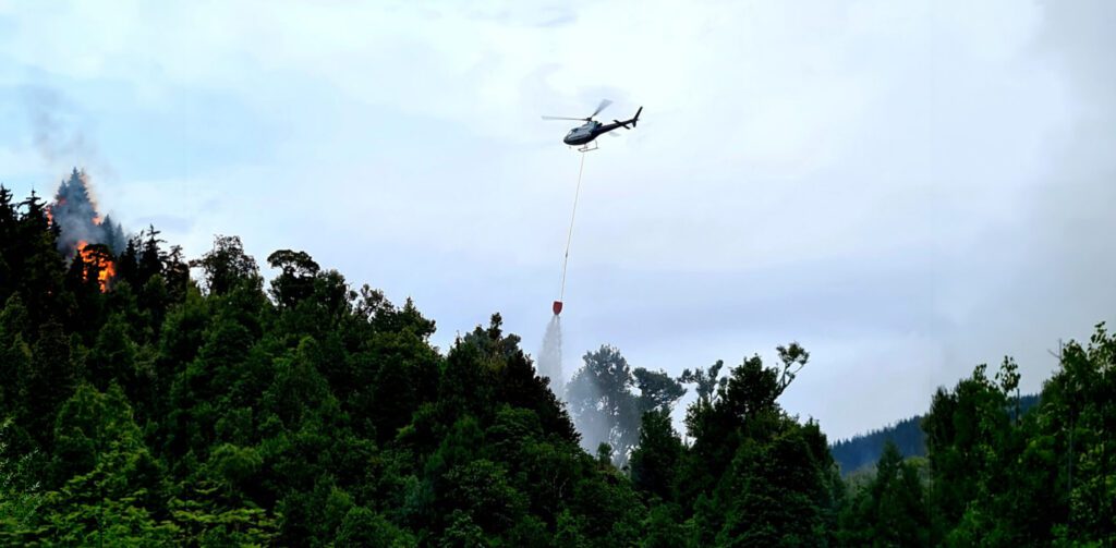 Helicopter conducting a targeted water drop on an active forest canopy wildfire.