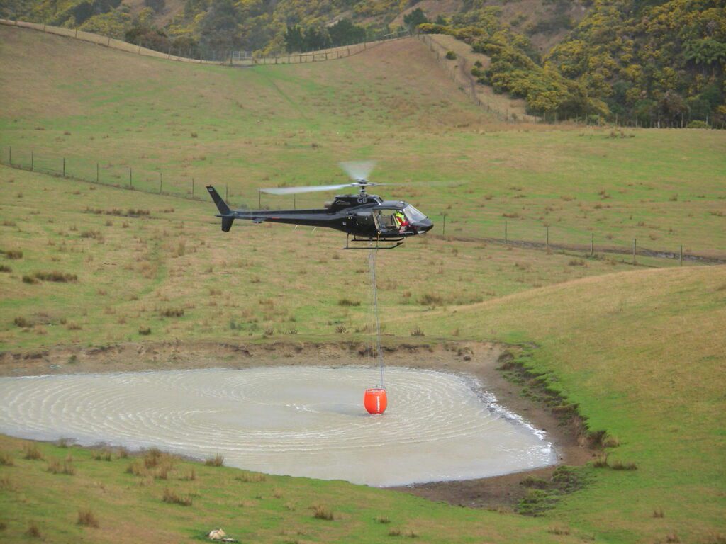 Aerial firefighting helicopter utilizing a long-line to hover-fill an underslung water bucket from a shallow pond