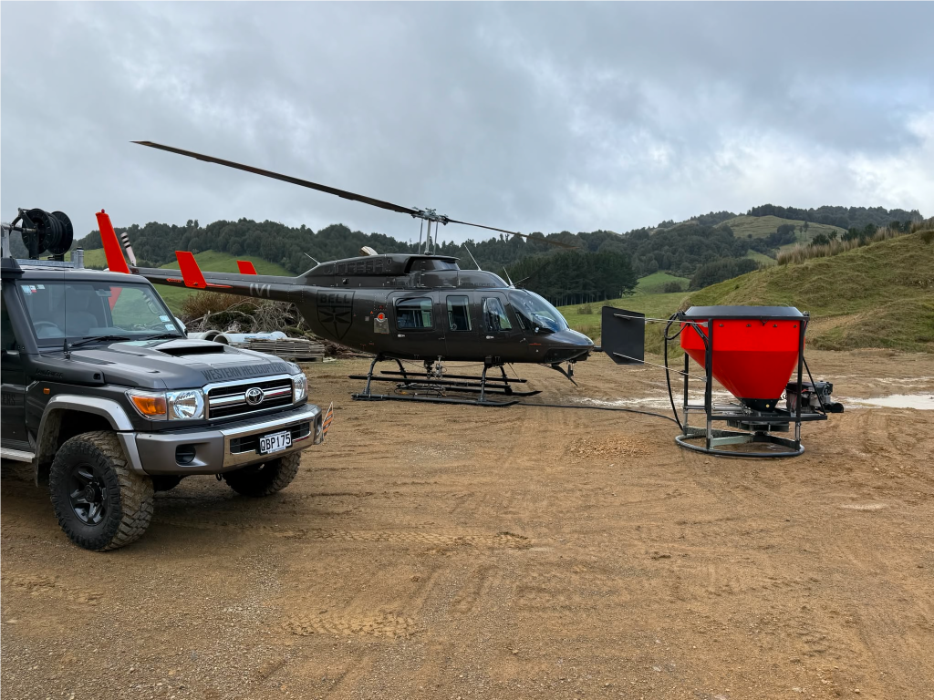 spreader bucket staged on the ground next to a utility helicopter and support vehicle