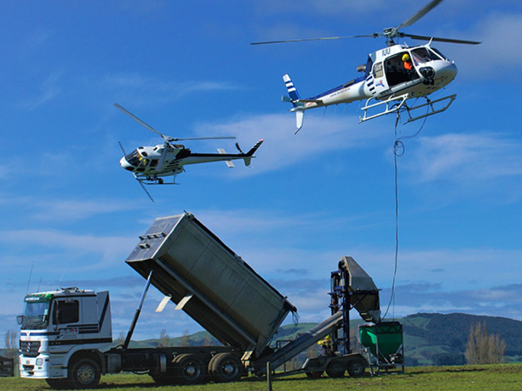 Two helicopters conducting a continuous loading operation with a Ground-Effect spreader bucket and a bulk transport truck